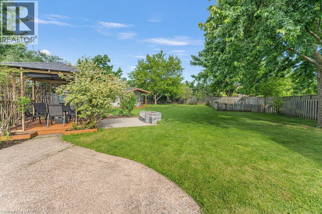 Expansive backyard featuring a lush lawn, concrete patio, and a built-in stone fire pit - 33 Remple Court, Cambridge, ON - Outdoor