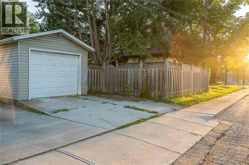 Detached garage with horizontal siding and a panel garage door, complemented by a wooden fence and mature trees - 41 Paradise Road S, Hamilton, ON - Outdoor