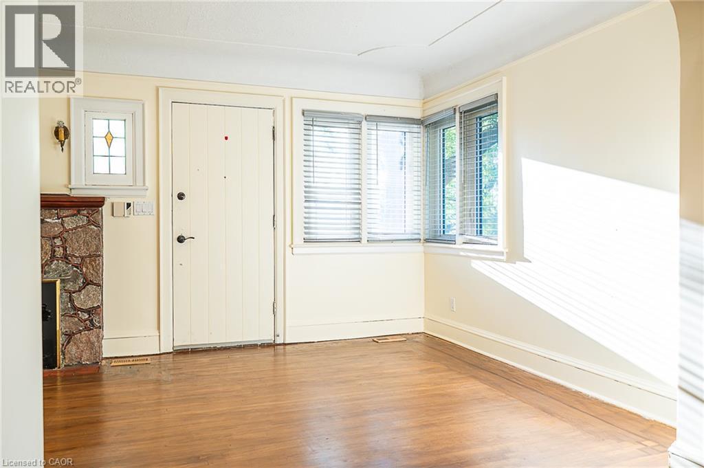 Hardwood flooring, stone fireplace with wood mantel, decorative stained glass window, multiple windows with blinds, and white entry door - 41 Paradise Road S, Hamilton, ON - Indoor Photo Showing Other Room