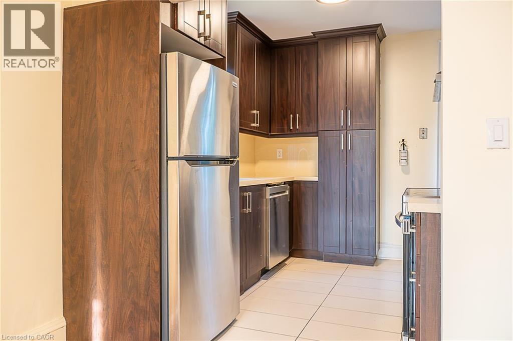 Stainless steel refrigerator, dark wood-finish cabinetry, light tile flooring, light-toned countertops, and a stainless steel dishwasher - 41 Paradise Road S, Hamilton, ON - Indoor Photo Showing Kitchen