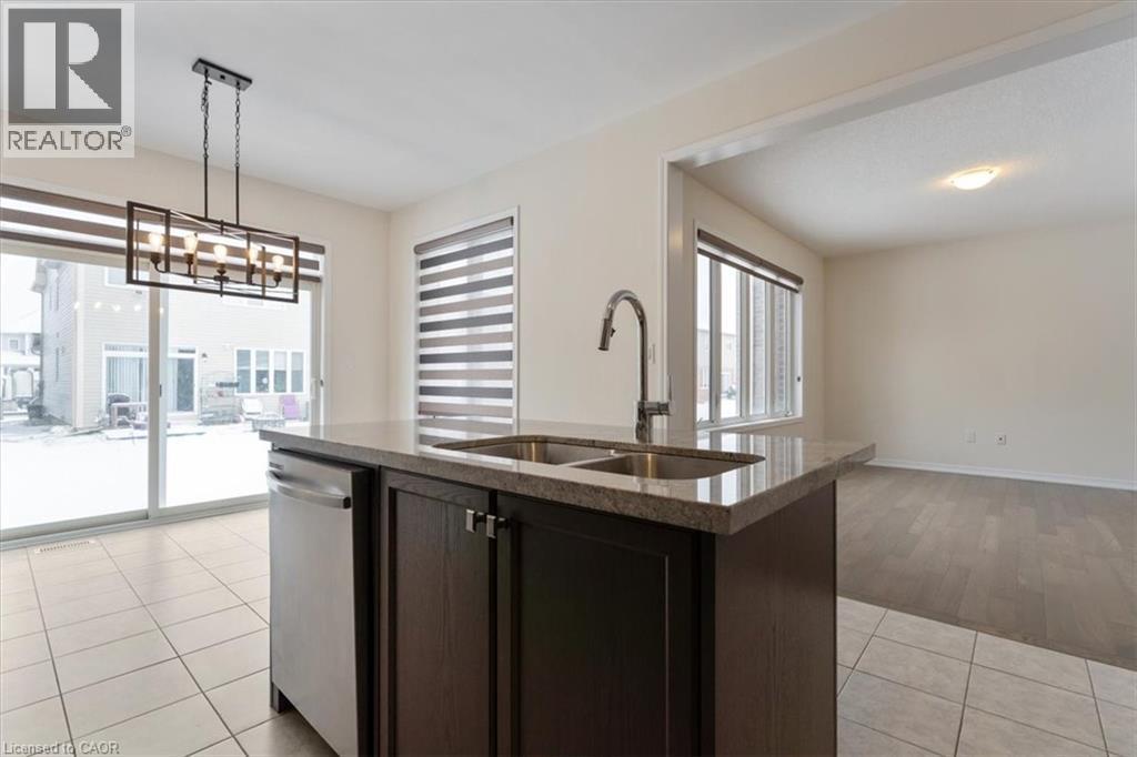 Kitchen featuring light tile patterned floors, stone countertops, dishwasher, open floor plan, and a sink - 13 Steven Drive, Thorold, ON - Indoor Photo Showing Kitchen With Double Sink