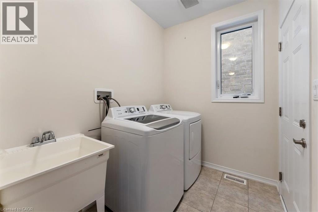 Clothes washing area with light tile patterned floors, washing machine and dryer, a sink, laundry area, and baseboards - 13 Steven Drive, Thorold, ON - Indoor Photo Showing Laundry Room
