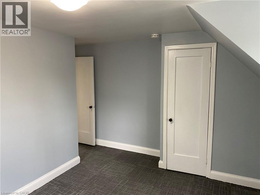 Light blue painted walls with white trim, two white paneled doors, textured gray carpet, and a flush mount ceiling light - 49 West Avenue, Kitchener, ON - Indoor Photo Showing Other Room