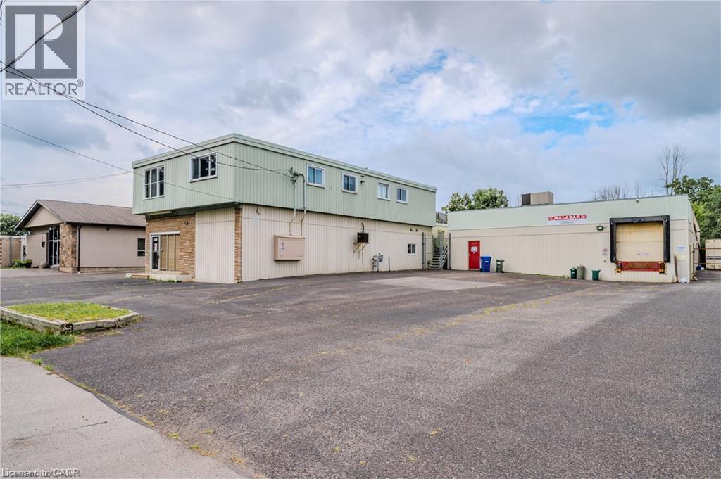 Expansive paved lot with multiple building structures, featuring a single loading dock and a brick facade entrance - 459 Enfield Road, Burlington, ON