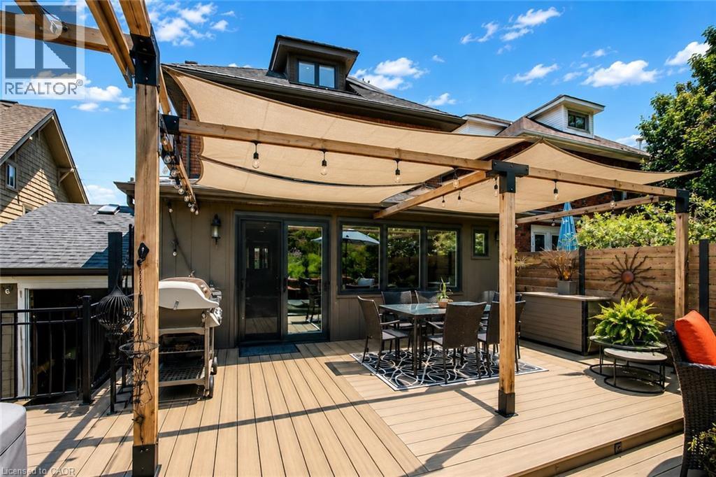 Expansive composite deck featuring a pergola with shade sails, outdoor string lighting, sliding glass door access, and a wood privacy fence - 99 Hillcrest Avenue, Hamilton, ON - Outdoor With Deck Patio Veranda With Exterior