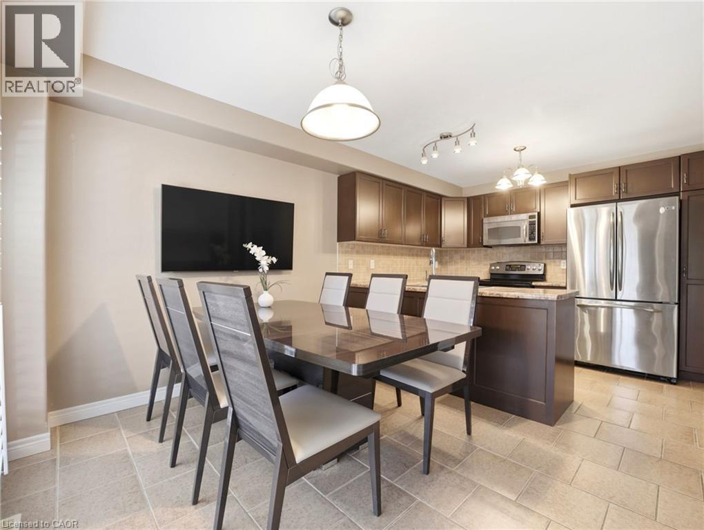 Open-concept kitchen and dining area featuring dark wood-finish cabinetry, stainless steel appliances, stone countertops, and tile flooring - 98 Willow Lane, Grimsby, ON - Indoor Photo Showing Dining Room