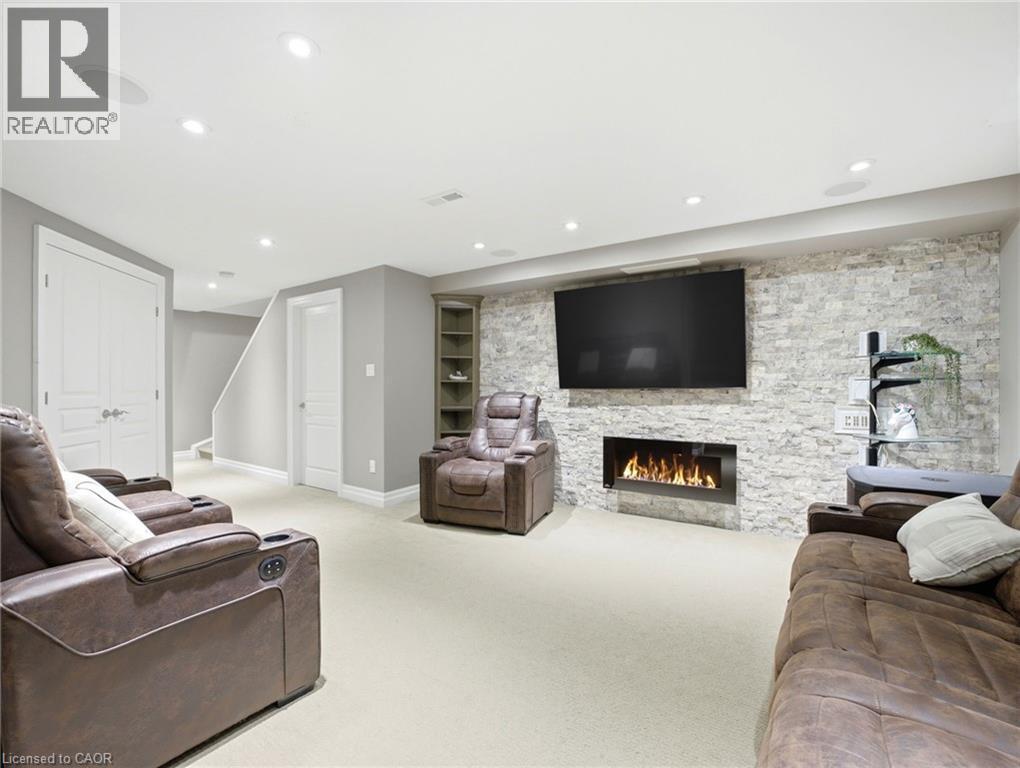 Entertainment room featuring a stone accent wall, linear fireplace, recessed lighting, and built-in shelving - 98 Willow Lane, Grimsby, ON - Indoor Photo Showing Living Room With Fireplace