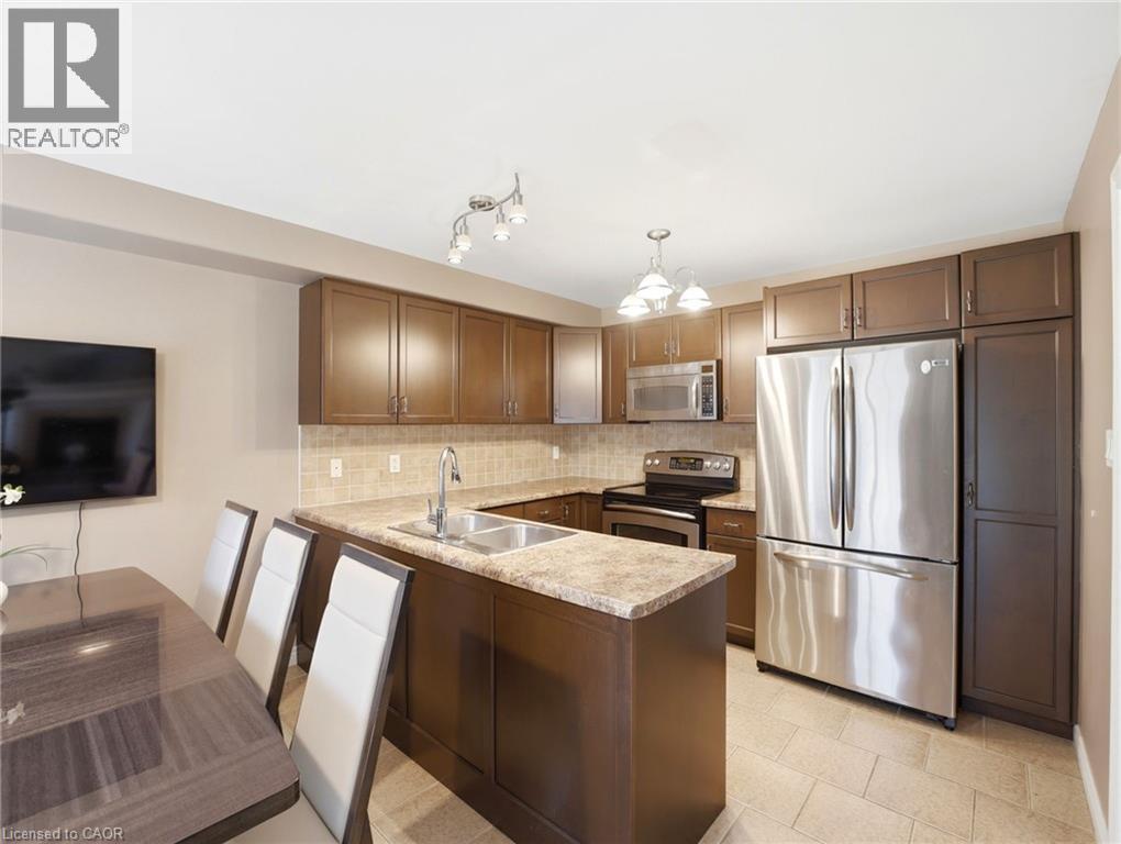 Kitchen featuring stainless steel appliances, dark wood cabinetry, a tiled backsplash, and light-toned countertops - 98 Willow Lane, Grimsby, ON - Indoor Photo Showing Kitchen With Stainless Steel Kitchen With Double Sink