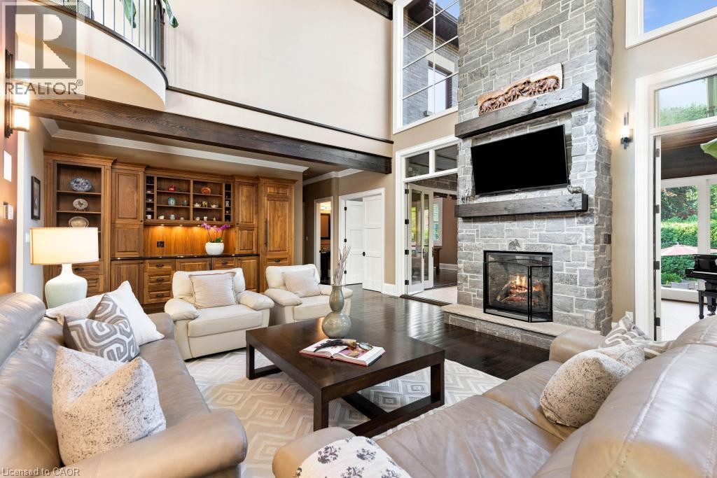 Expansive living area featuring a floor-to-ceiling stone fireplace, rich wood-finish flooring, built-in cabinetry with integrated lighting, and a two-story ceiling with exposed beams - 253 Rossmore Boulevard, Burlington, ON - Indoor Photo Showing Living Room With Fireplace