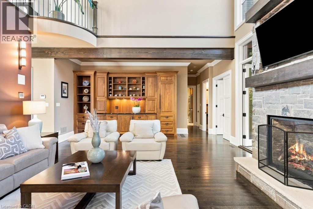 Hardwood flooring, stone-clad fireplace with hearth, built-in cabinetry, exposed wood beam, and an upper-level balcony with metal railings - 253 Rossmore Boulevard, Burlington, ON - Indoor Photo Showing Living Room With Fireplace