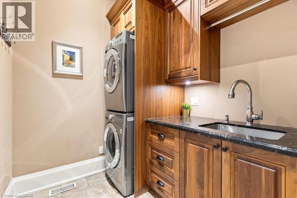 Laundry area featuring a stackable washer and dryer, wood-finish cabinetry, a sink with a gooseneck faucet, and a dark stone countertop - 253 Rossmore Boulevard, Burlington, ON - Indoor Photo Showing Laundry Room