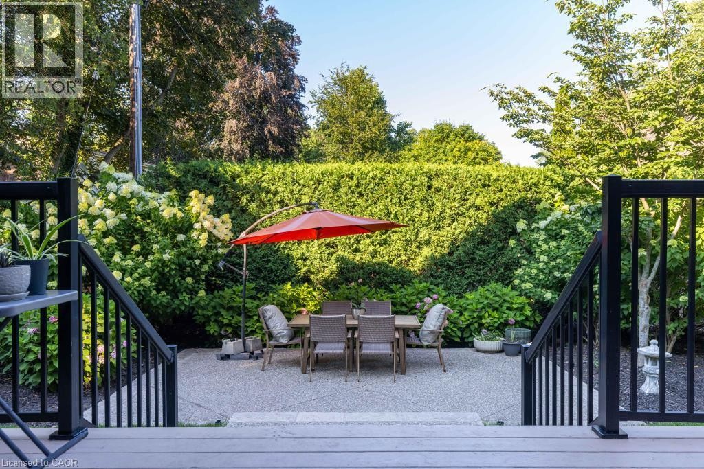Expansive patio with textured concrete, framed by lush perimeter plantings and a mature hedge - 253 Rossmore Boulevard, Burlington, ON - Outdoor