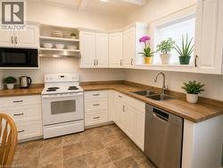 White shaker-style cabinetry, warm wood-finish countertops, a stainless steel double sink and dishwasher, and tiled flooring create a bright and welcoming kitchen. - 