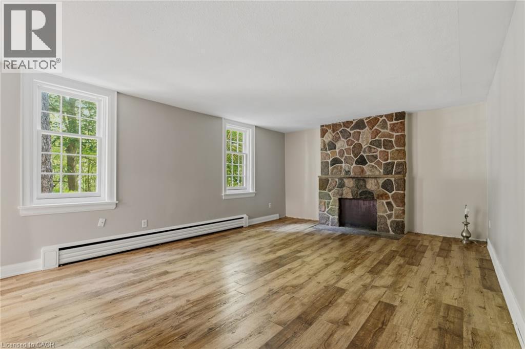 Expansive interior space featuring a floor-to-ceiling stone fireplace, wood-finish flooring, and multiple double-hung windows - 41 Mill Street, Mississauga, ON - Indoor Photo Showing Living Room With Fireplace