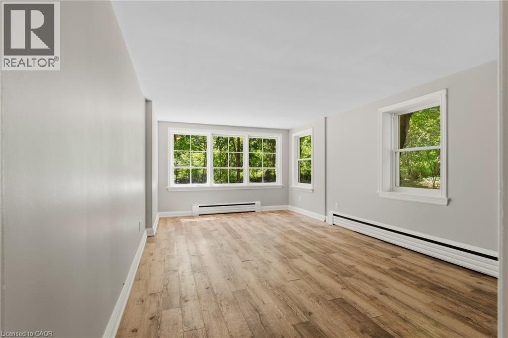 Spacious room featuring wood-finish flooring, light grey walls, and multiple windows with white trim - 41 Mill Street, Mississauga, ON - Indoor