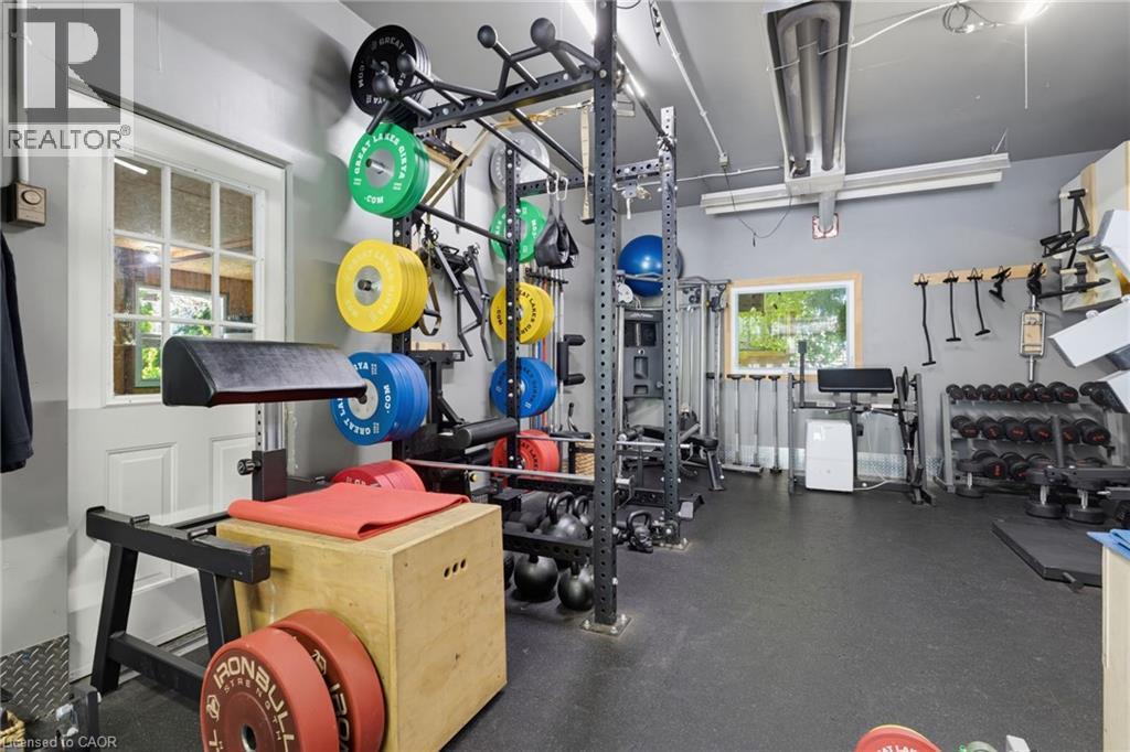 Dedicated Home Gym featuring a comprehensive strength training setup with wall-mounted weight storage, Olympic barbell rack system, adjustable dumbbell collection, and rubber-finish flooring throughou - 21 Kerman Avenue, Grimsby, ON
