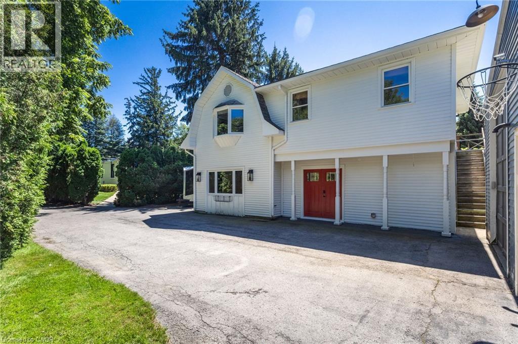 Contemporary home featuring a clean white exterior with architectural gable detailing, two-car garage with roll-up doors, and a spacious asphalt driveway - 21 Kerman Avenue, Grimsby, ON