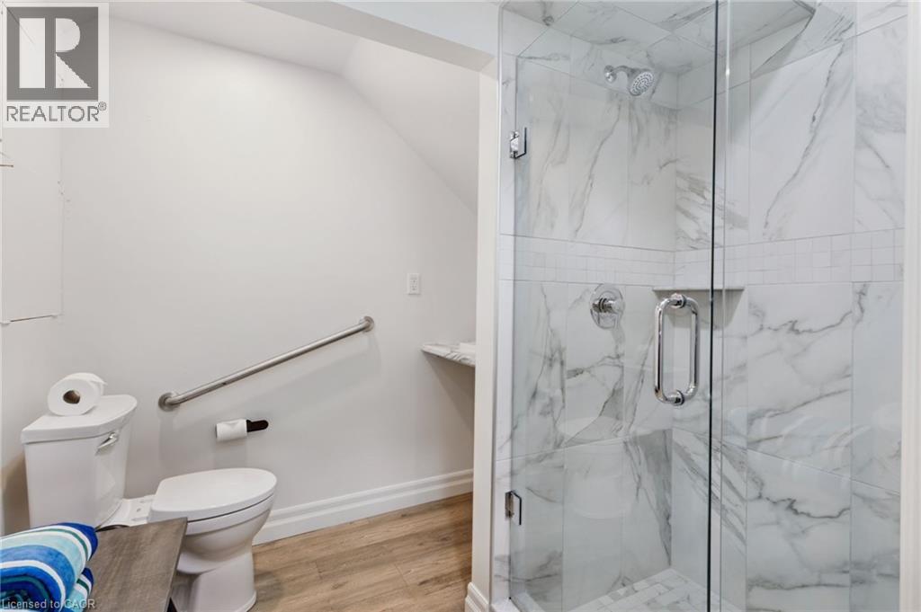 Walk-in shower with clear glass enclosure, marble-patterned tile, and chrome fixtures - 21 Kerman Avenue, Grimsby, ON