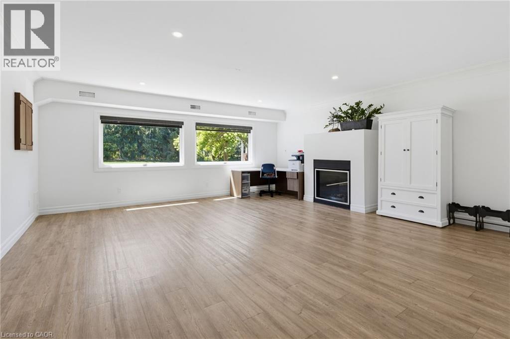Bright, open living space featuring wood-finish flooring throughout, dual casement windows with natural light, built-in fireplace with surround, and white cabinetry with integrated storage - 21 Kerman Avenue, Grimsby, ON