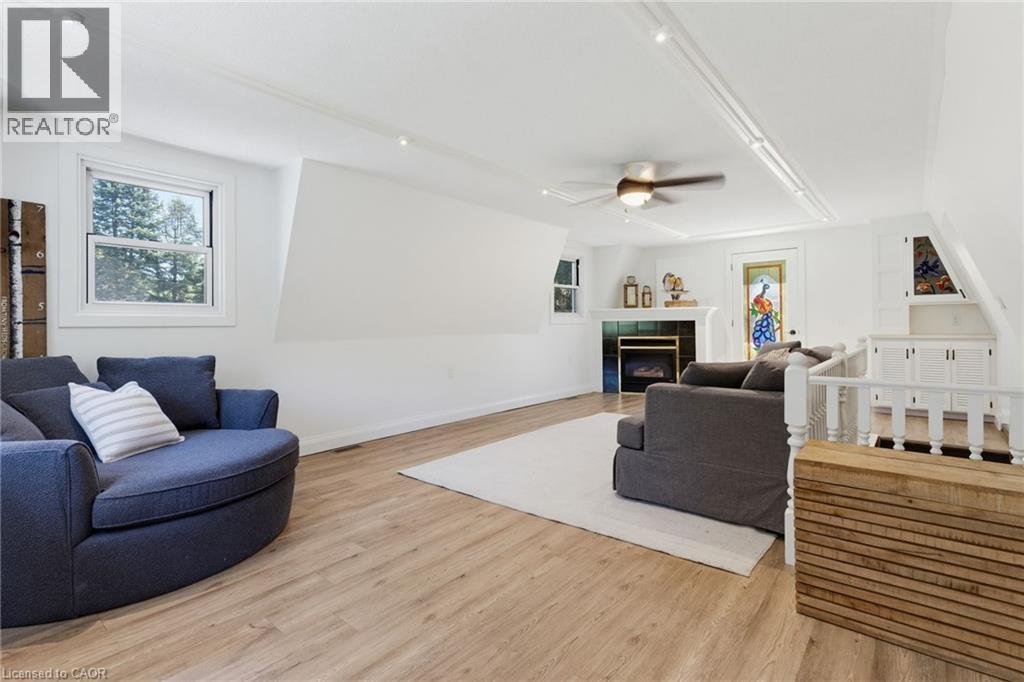 Open-concept living space featuring wood-finish flooring, a ceiling fan, a fireplace with a white mantel, and built-in cabinetry - 21 Kerman Avenue, Grimsby, ON