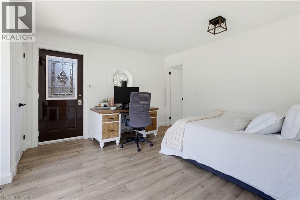 Bright bedroom with wood-finish flooring, abundant natural light from multiple windows, and a dedicated workspace featuring a desk with storage cabinetry and task seating - 21 Kerman Avenue, Grimsby, ON