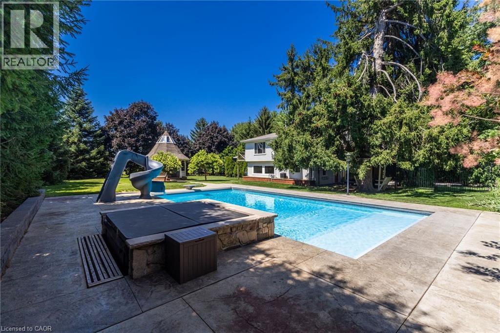 Resort-style backyard oasis featuring a sparkling in-ground swimming pool with sun lounging area, mature landscaping with privacy trees, modern patio hardscaping, and a two-story residence set on expa - 21 Kerman Avenue, Grimsby, ON