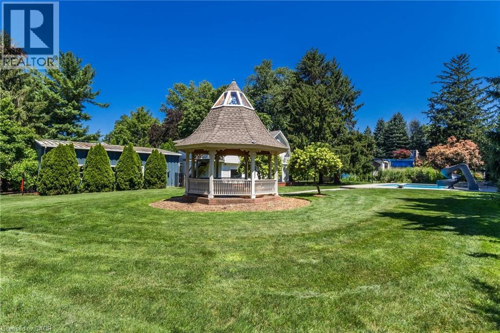 Expansive lawn featuring a gazebo with a shingled roof, mature trees, and a swimming pool - 21 Kerman Avenue, Grimsby, ON
