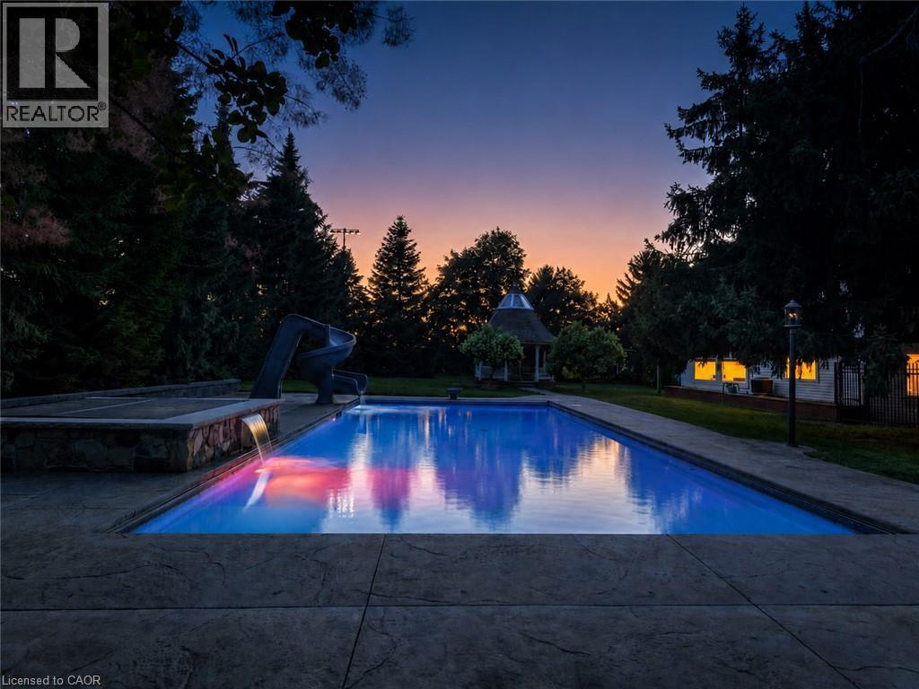 Rectangular swimming pool with integrated slide, adjacent stone-clad water feature, and stamped concrete decking - 21 Kerman Avenue, Grimsby, ON
