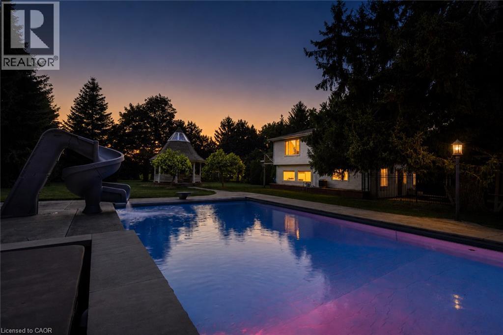 Expansive outdoor swimming pool with integrated slide, surrounded by a manicured lawn and mature trees - 21 Kerman Avenue, Grimsby, ON