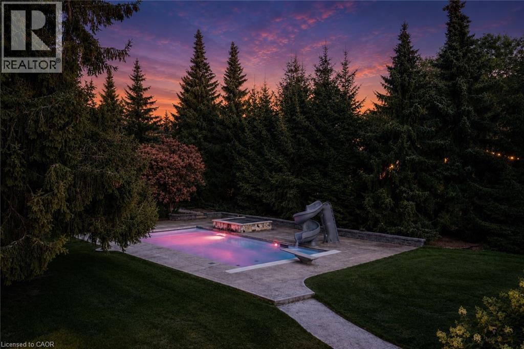 Swimming pool with integrated slide, surrounded by a stone patio and manicured lawn - 21 Kerman Avenue, Grimsby, ON