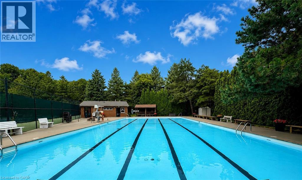 Outdoor swimming pool with integrated lane lines, surrounded by a paved deck and mature perimeter landscaping - 119 Sandy Ridge Place, Waterloo, ON - Outdoor With In Ground Pool With Backyard