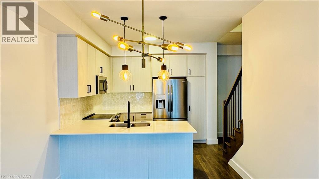 Modern kitchen featuring light-toned cabinetry, stainless steel appliances, a bar-height counter, and an angular chandelier - 1159 Lloyd Landing, Milton, ON - Indoor Photo Showing Kitchen With Double Sink