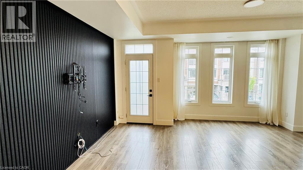 Wood-finish flooring, accent wall with vertical paneling, three tall windows, and a glass-paneled door - 1159 Lloyd Landing, Milton, ON - Indoor Photo Showing Other Room