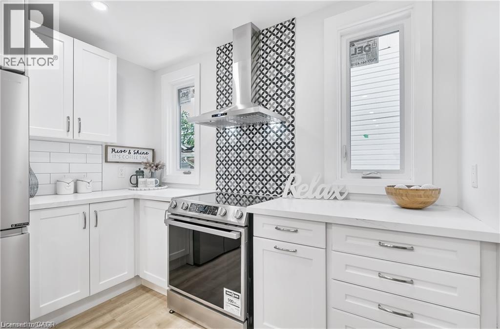 Modern kitchen featuring white cabinetry, light countertops, stainless steel appliances, a geometric patterned backsplash, and wood-finish flooring - 10 Comet Avenue Unit# #1 (Main), Hamilton, ON - Indoor Photo Showing Kitchen