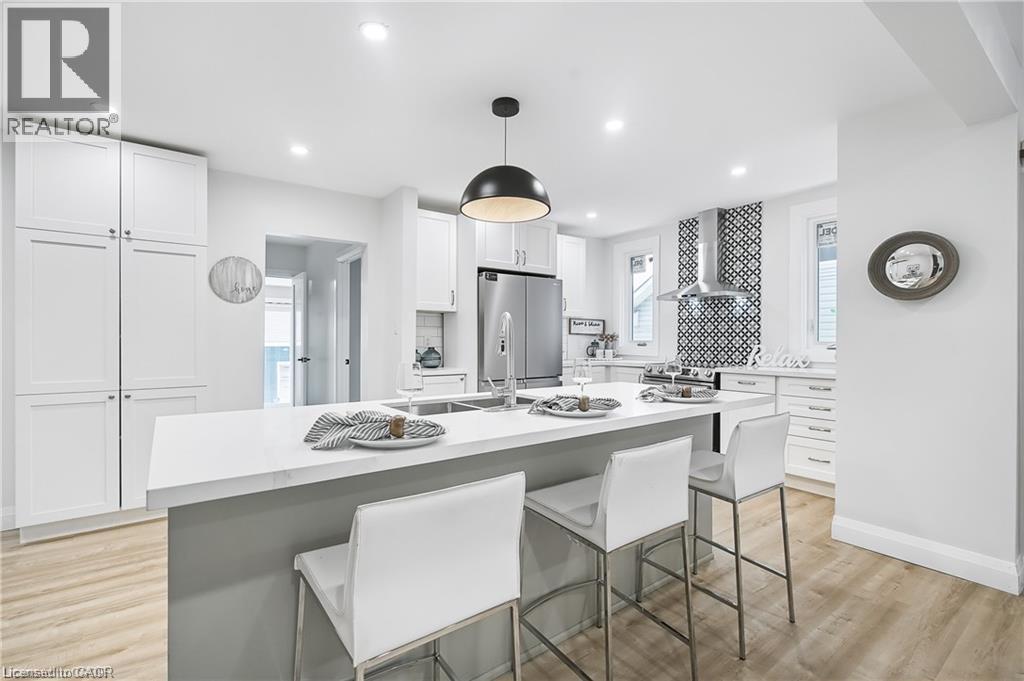 Bright kitchen featuring a central island with countertop seating, stainless steel appliances, a geometric pattern tile backsplash, recessed lighting, and wood-finish flooring - 10 Comet Avenue Unit# #1 (Main), Hamilton, ON - Indoor
