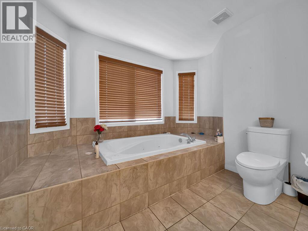 Built-in jetted tub surrounded by large format tile, complemented by a white toilet - 227 Baldwin Drive Unit# Main, Cambridge, ON - Indoor Photo Showing Bathroom