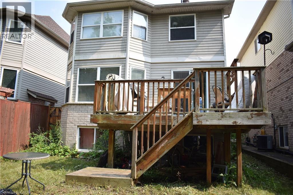 Rear elevation with light-toned horizontal siding, bay window extension, and a wooden deck with railing and stairs to the yard - 720 Brookmill Place, Waterloo, ON - Outdoor