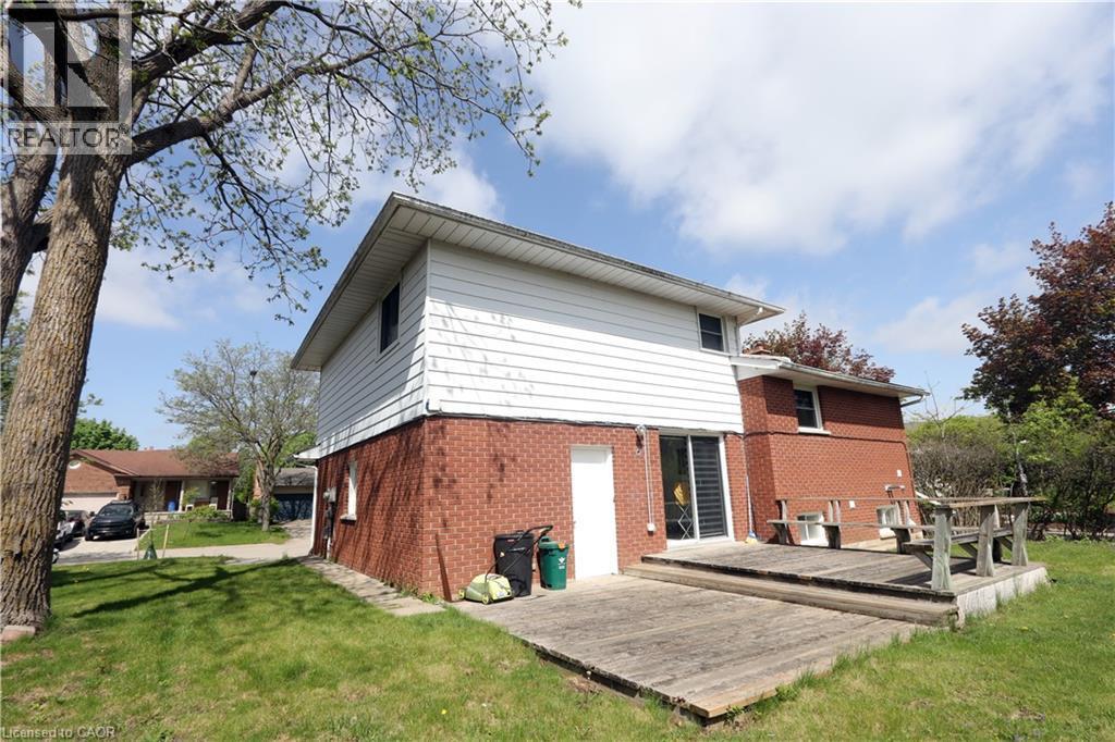 Expansive lawn area with mature trees, brick and siding exterior, sliding glass door access, and a wood deck - 77 Orchard Mill Crescent, Kitchener, ON - Outdoor With Exterior