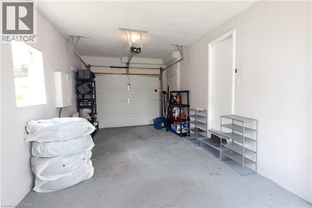 Attached garage with a white overhead door, finished walls, and concrete flooring - 77 Orchard Mill Crescent, Kitchener, ON - Indoor Photo Showing Garage
