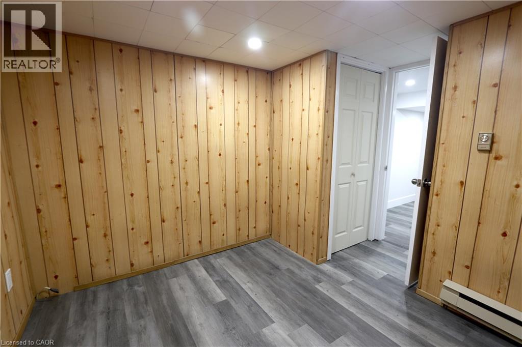 Wood-finish wall paneling, recessed ceiling lighting, wood-finish flooring, white bi-fold closet door, and baseboard heater - 77 Orchard Mill Crescent, Kitchener, ON - Indoor Photo Showing Other Room