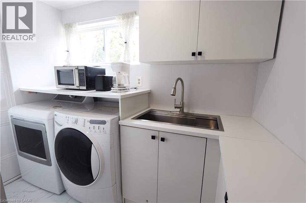 White cabinetry with black hardware, stainless steel sink, and white countertop - 77 Orchard Mill Crescent, Kitchener, ON - Indoor Photo Showing Laundry Room