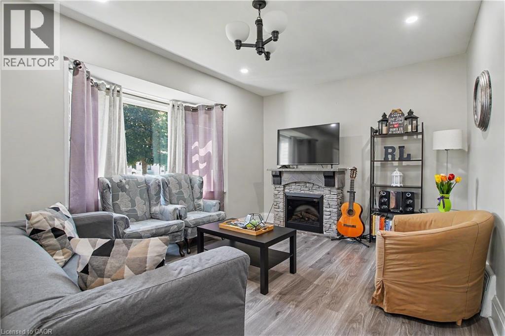 Spacious living area featuring wood-finish flooring, a stone-clad fireplace with mantel, recessed lighting, and a prominent bay window - 16 Mercer Road, Cambridge, ON - Indoor Photo Showing Living Room With Fireplace