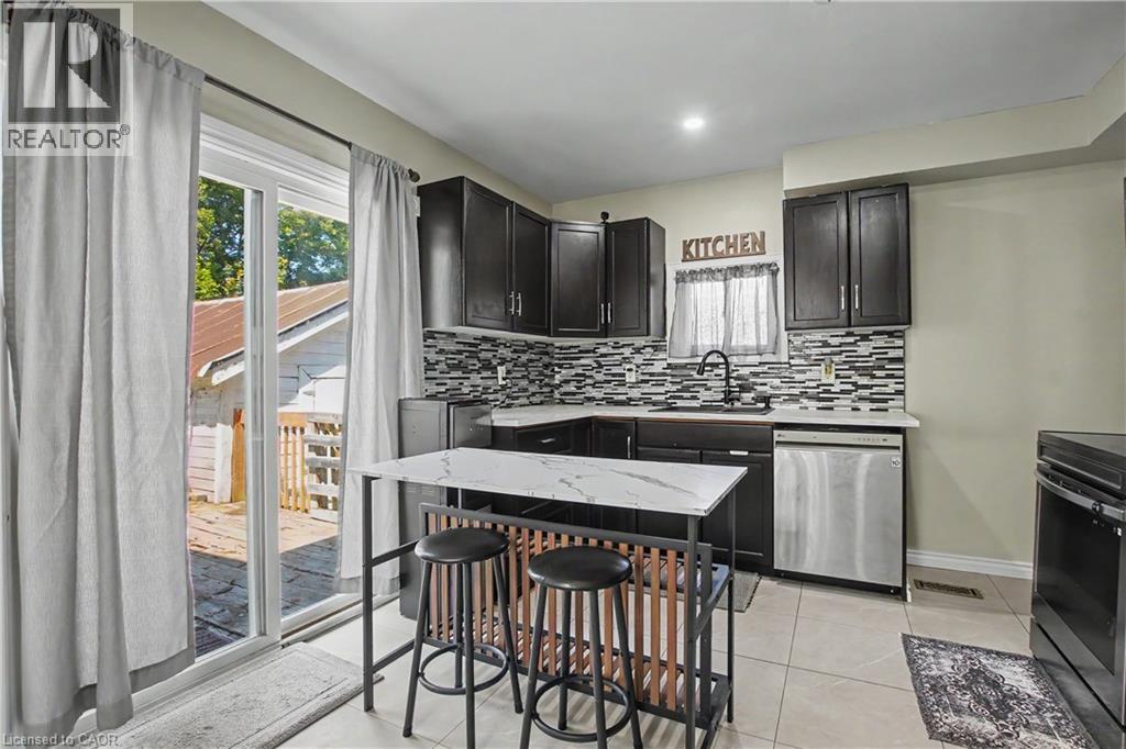 Updated kitchen featuring dark wood cabinetry, a mosaic tile backsplash, stainless steel appliances, and a sliding glass door - 16 Mercer Road, Cambridge, ON - Indoor