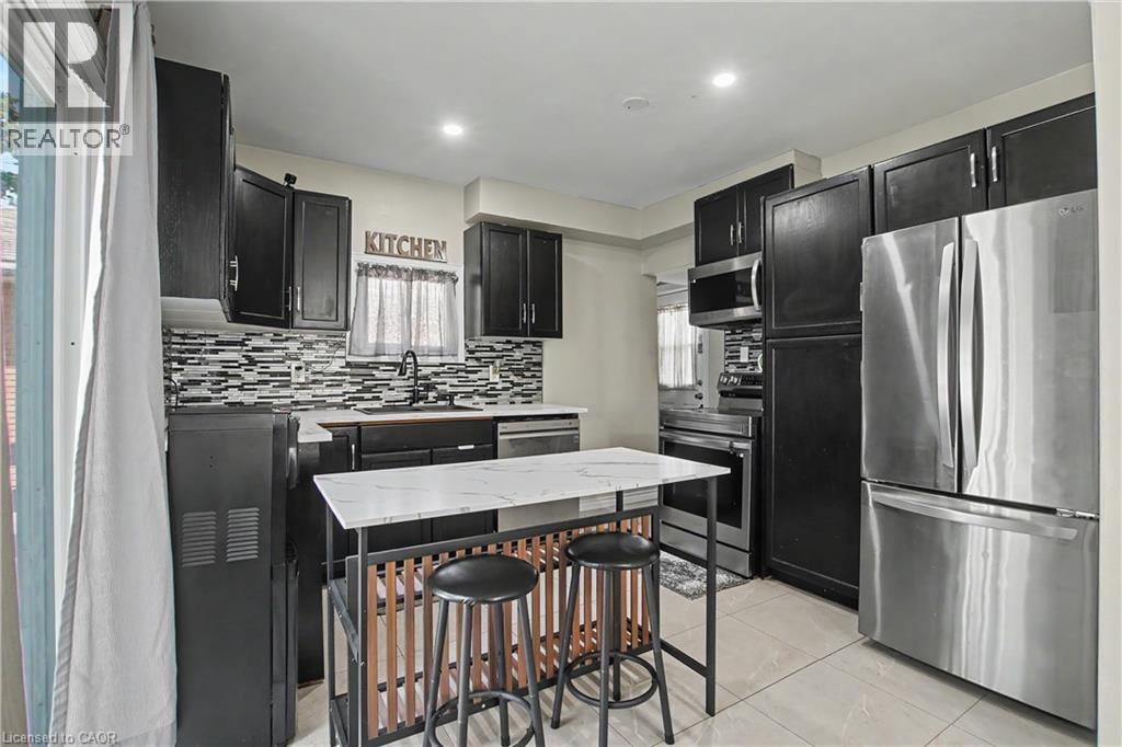 Modern kitchen featuring dark cabinetry, stainless steel appliances, a mosaic tile backsplash, and a central island with a stone-finish countertop - 16 Mercer Road, Cambridge, ON - Indoor