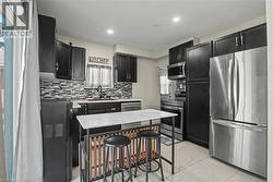 Modern kitchen featuring dark cabinetry, stainless steel appliances, a mosaic tile backsplash, and a central island with a stone-finish countertop -