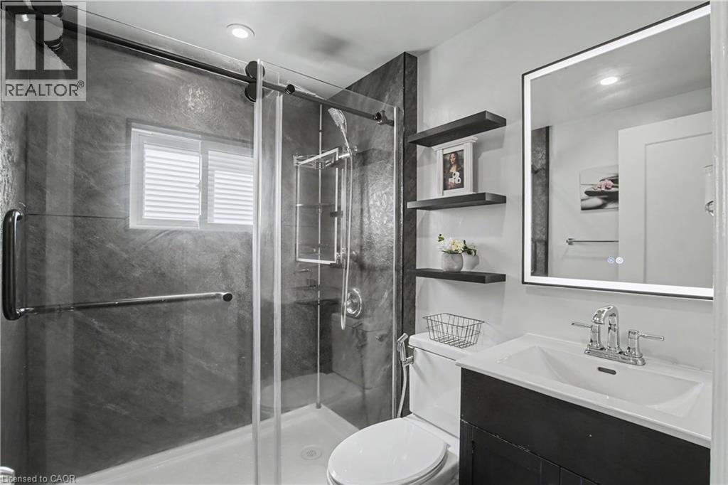 Frameless glass shower enclosure with sliding door, dark stone-finish shower walls, window with blinds, illuminated mirror, and floating shelving - 16 Mercer Road, Cambridge, ON - Indoor Photo Showing Bathroom
