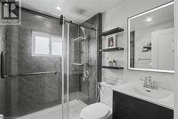 Frameless glass shower enclosure with sliding door, dark stone-finish shower walls, window with blinds, illuminated mirror, and floating shelving -