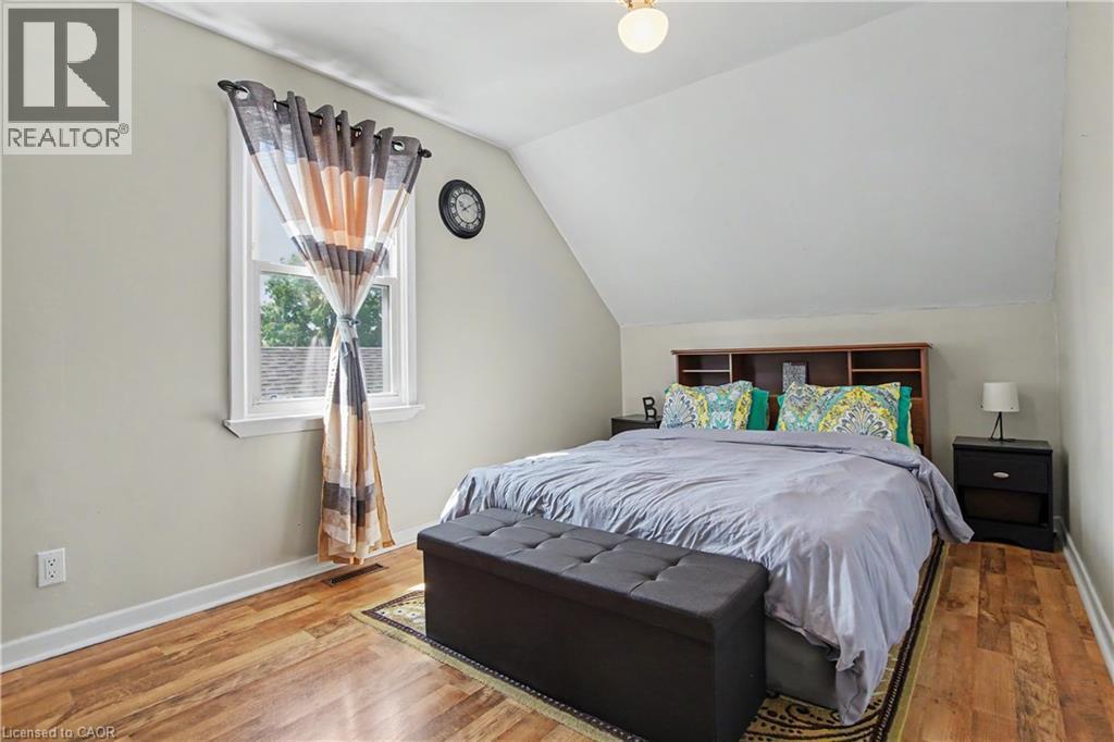 Sloped ceiling bedroom featuring wood-finish flooring, a double-hung window, and a built-in headboard with shelving - 16 Mercer Road, Cambridge, ON - Indoor Photo Showing Bedroom