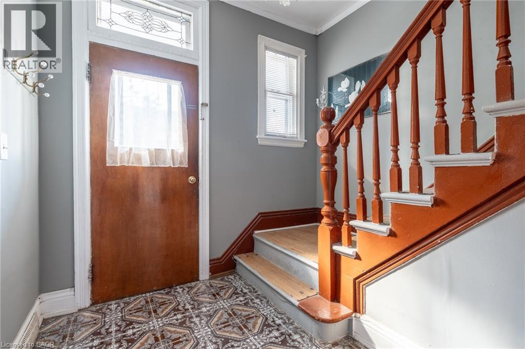 Entry foyer with patterned floor tiles, wood-finish door with decorative transom window, and a wood-finish staircase with balusters - 128 Hess Street N, Hamilton, ON - Indoor Photo Showing Other Room