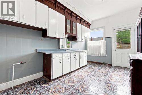 Kitchen featuring patterned tile flooring, white cabinetry, dark wood trim, a single basin sink, and a rear door - 128 Hess Street N, Hamilton, ON - Indoor Photo Showing Kitchen